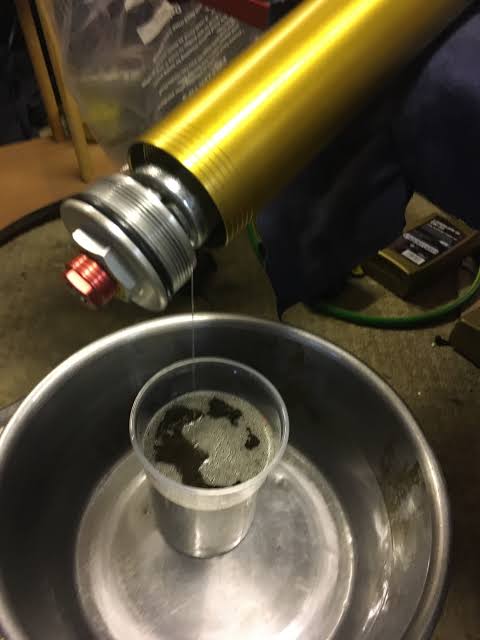 Draining old motorcycle fork oil into a workshop drain container